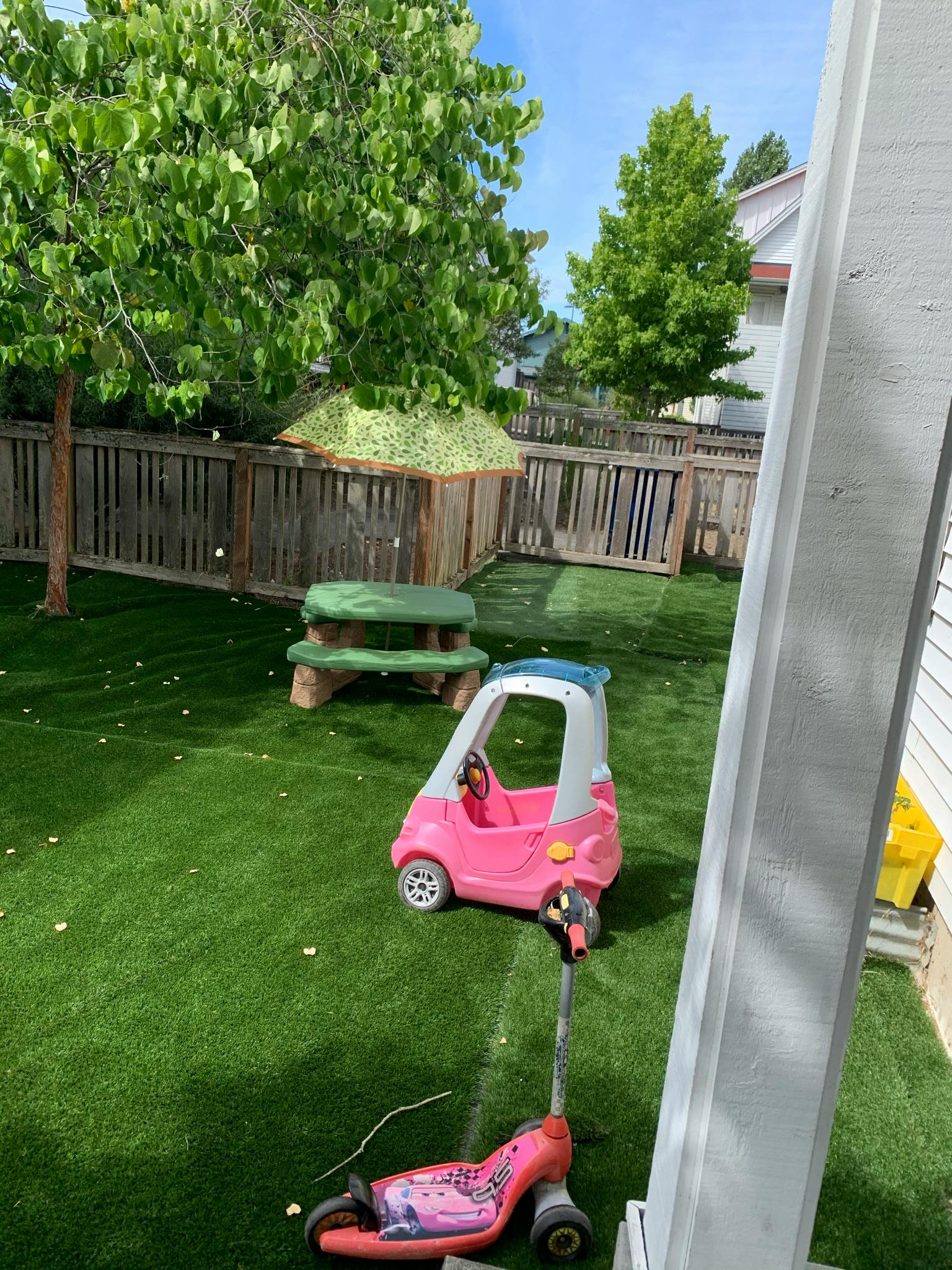 Pink toy car and scooter on green grass in a fenced yard