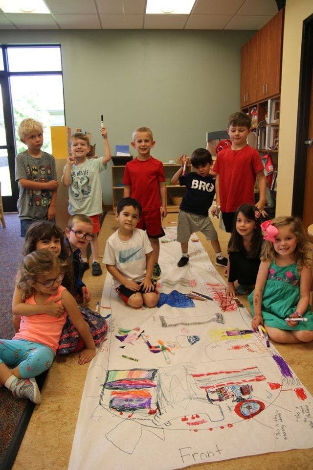 Group of children standing and sitting around a large drawing on the floor