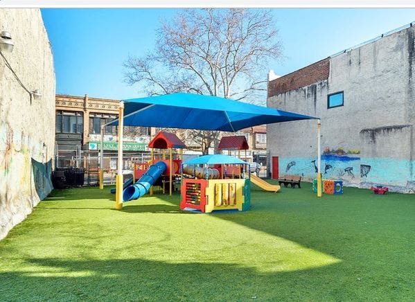 Outdoor playground with artificial turf, slides, and a blue shade canopy