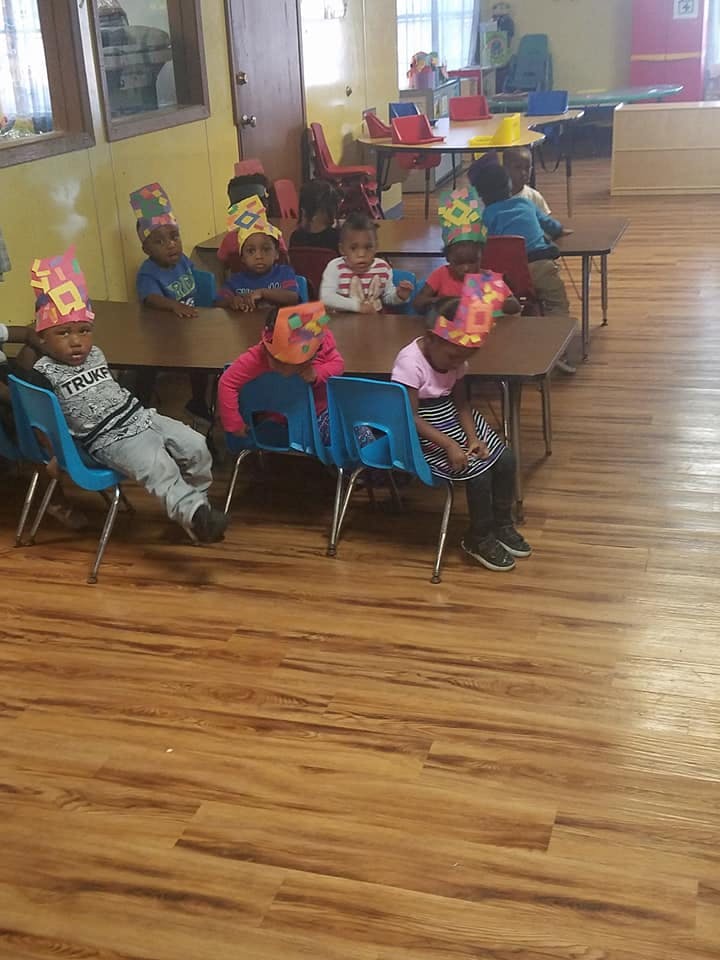 Children wearing paper crowns sitting at tables in a classroom