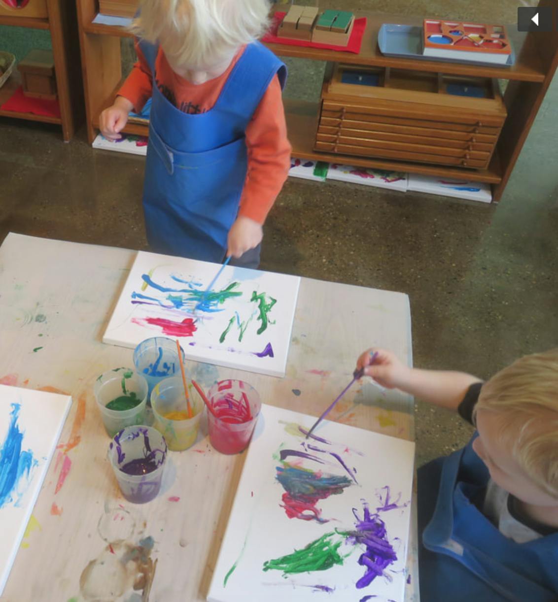 Two children painting on canvases at a table