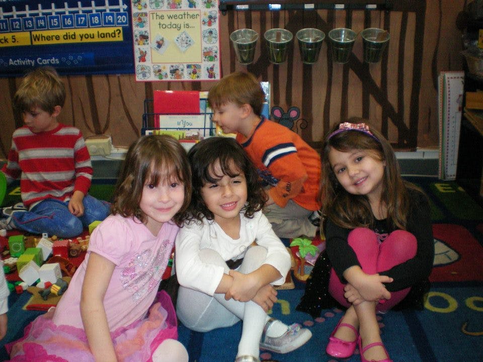 Three children sitting on a rug, two children in the background