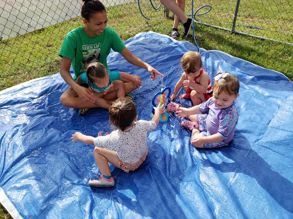 Person and three children playing with water on a blue tarp