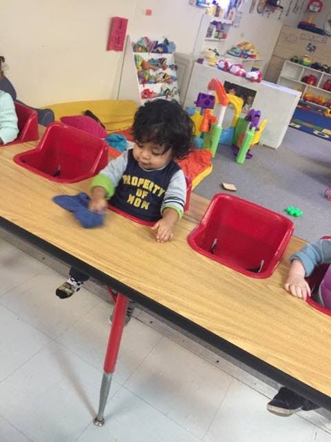 Child sitting at a table with red seats, holding a blue object