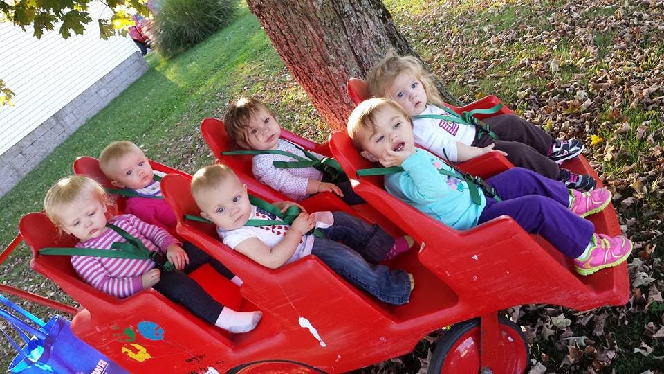 Multiple children sitting in a red multi-seat wagon