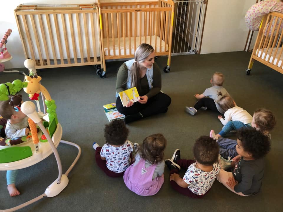 Person reading a book to a group of children sitting on the floor