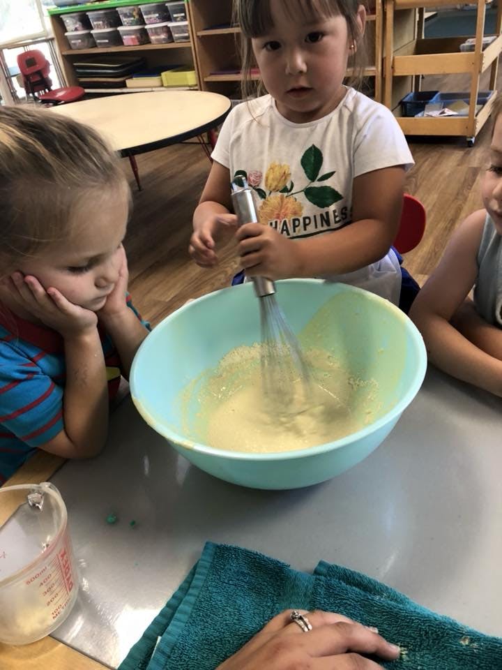 Child whisking batter in a bowl with another child watching