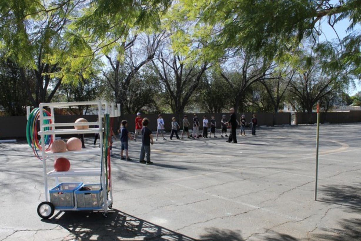 Children playing on a paved area with a cart of sports equipment
