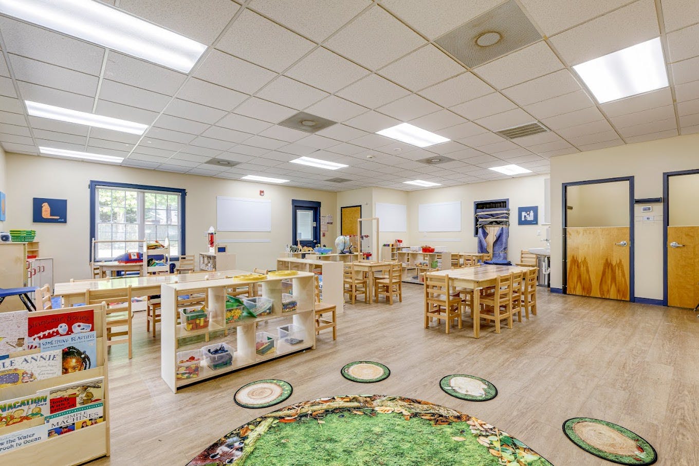 Classroom with small wooden tables and chairs, shelves with toys, and whiteboards