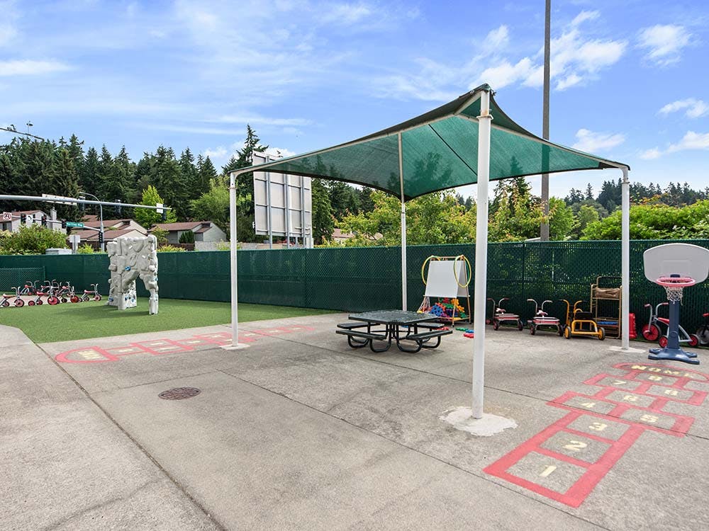 Outdoor play area with a climbing wall, tricycles, hopscotch, and a basketball hoop