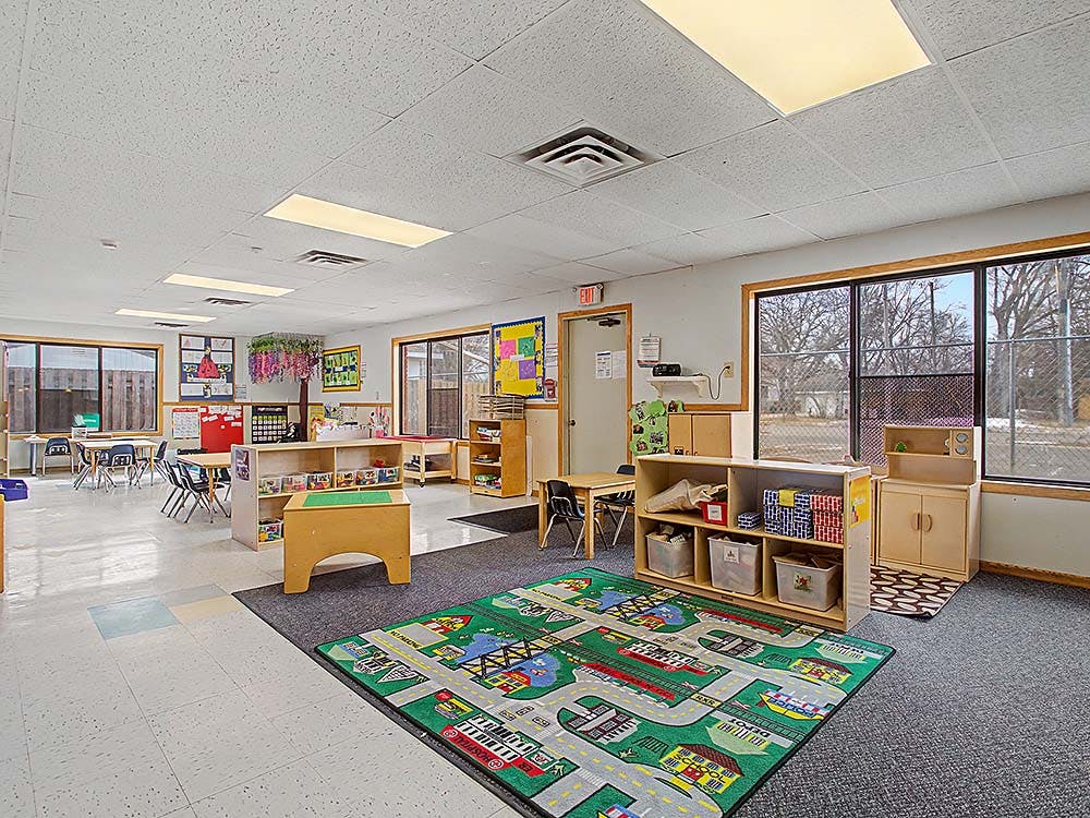 Classroom with tables, chairs, shelving units, and a colorful rug
