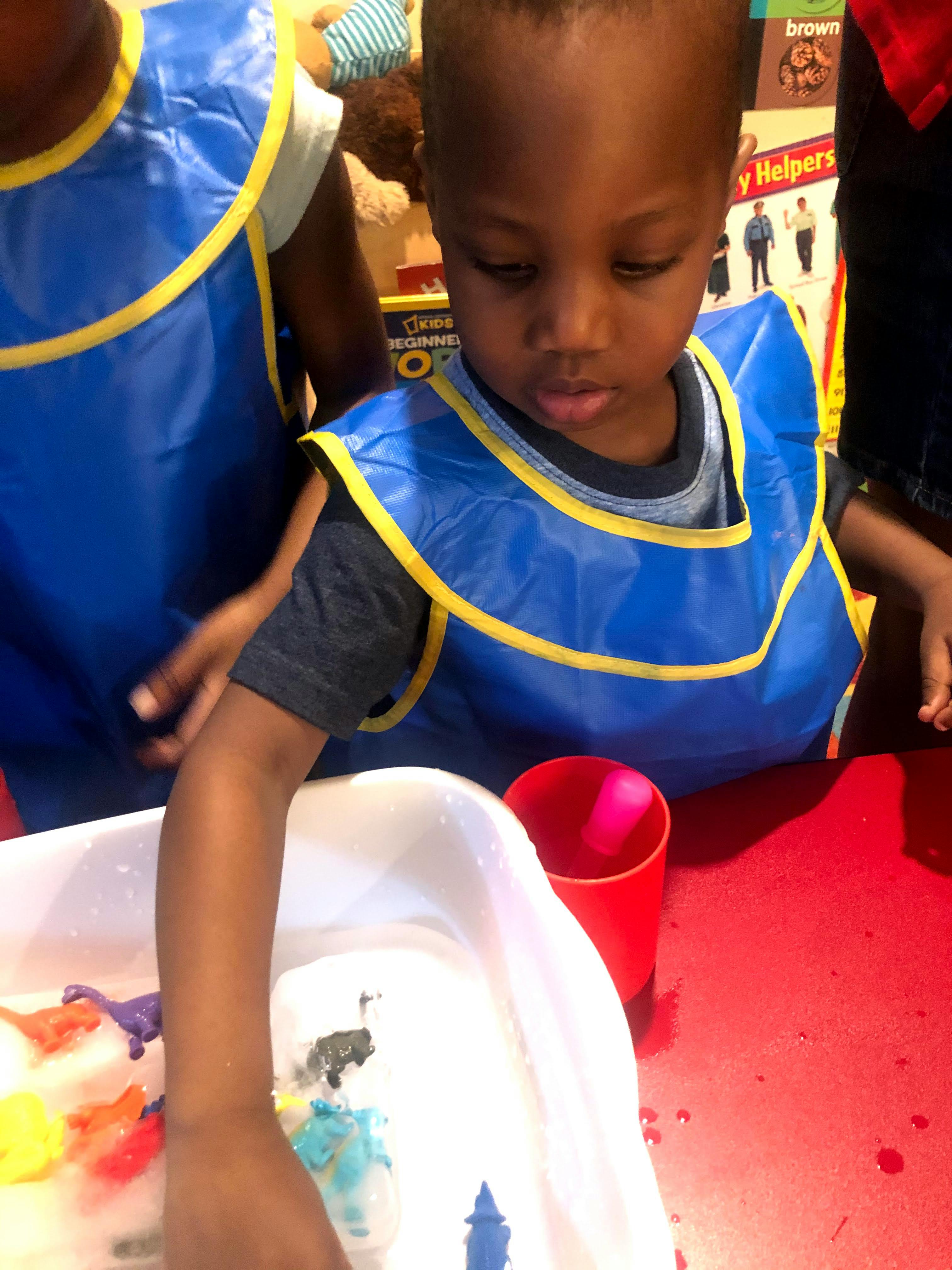 Child in a blue smock playing with toys in a white bin