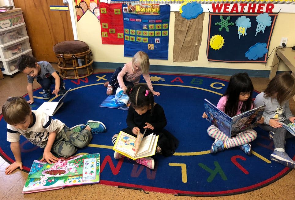 Children reading books on a rug in a classroom