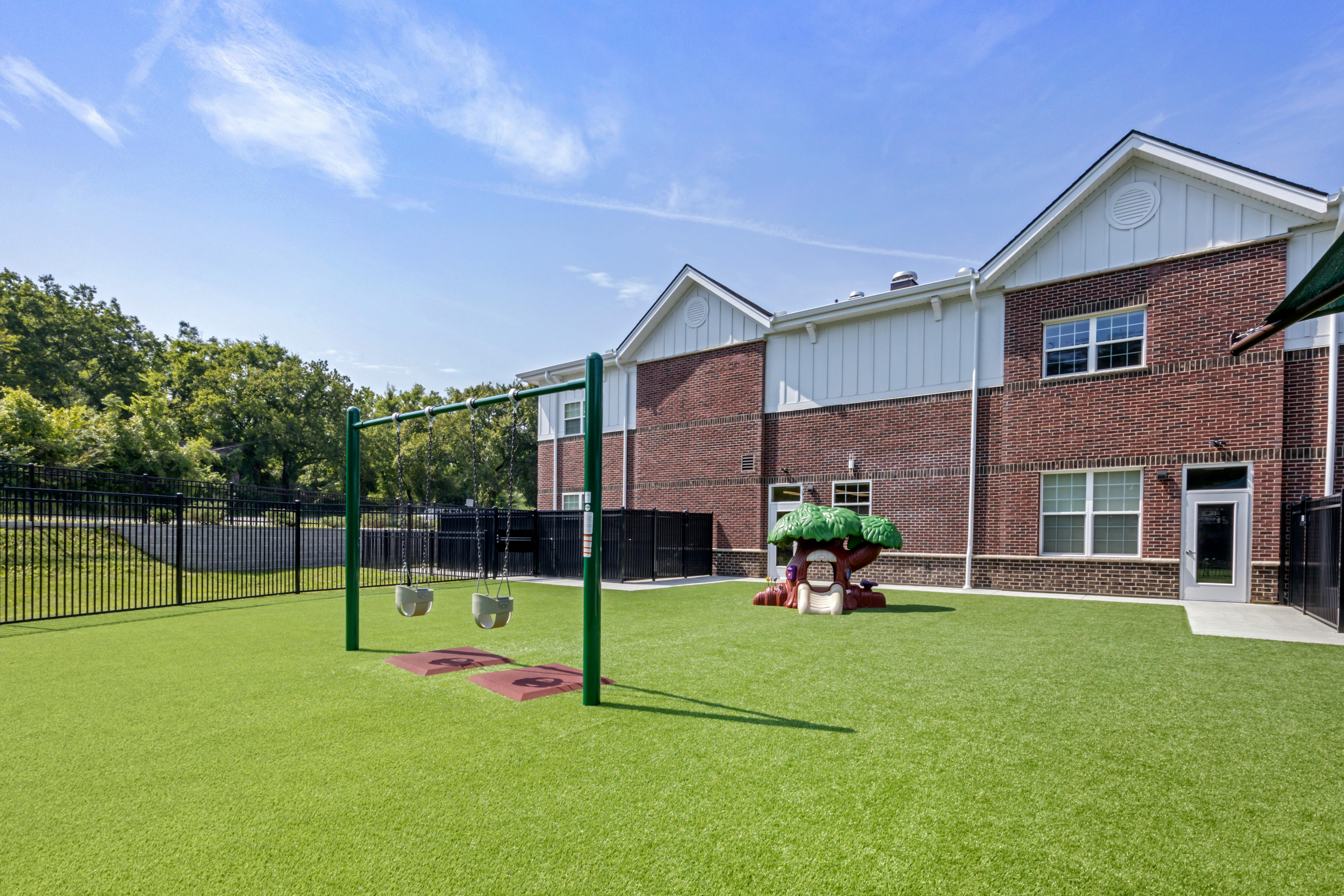 Playground with swings, a treehouse slide, and a brick building