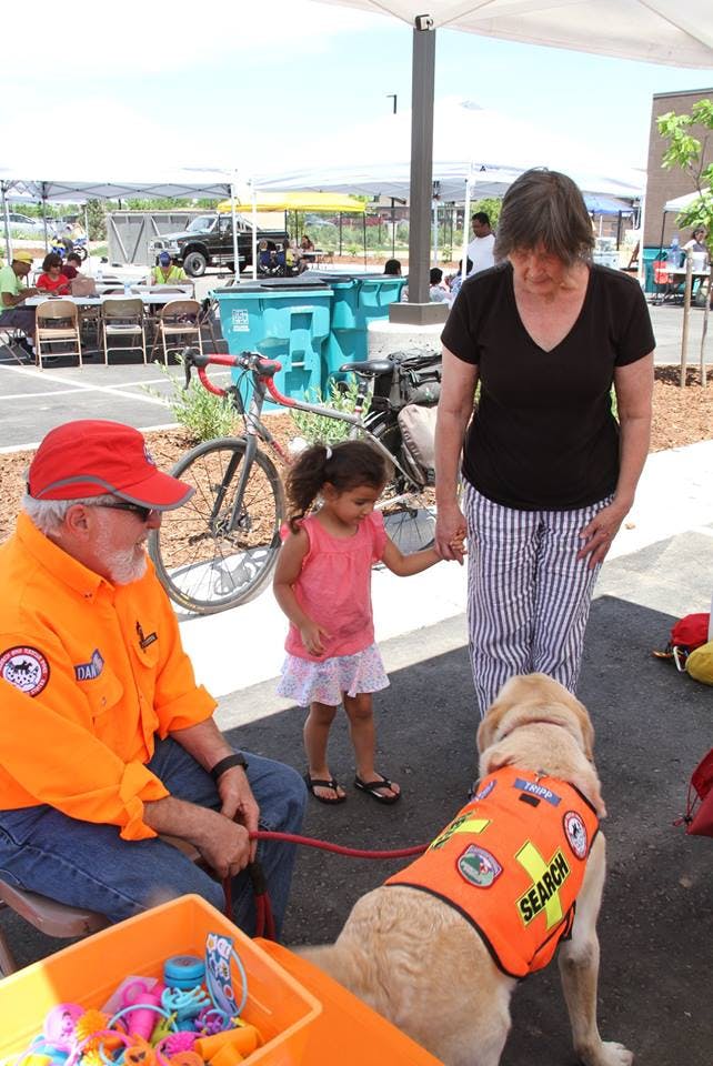 Person in orange shirt holding a dog on a leash, child and person standing nearby