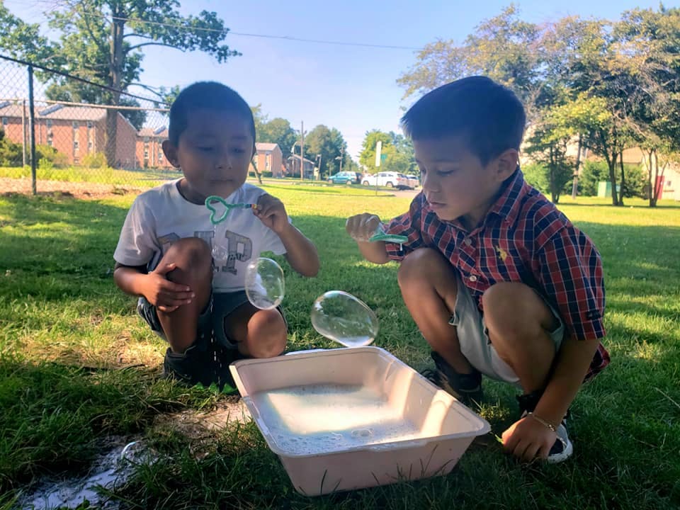 Two children squatting and blowing bubbles outdoors
