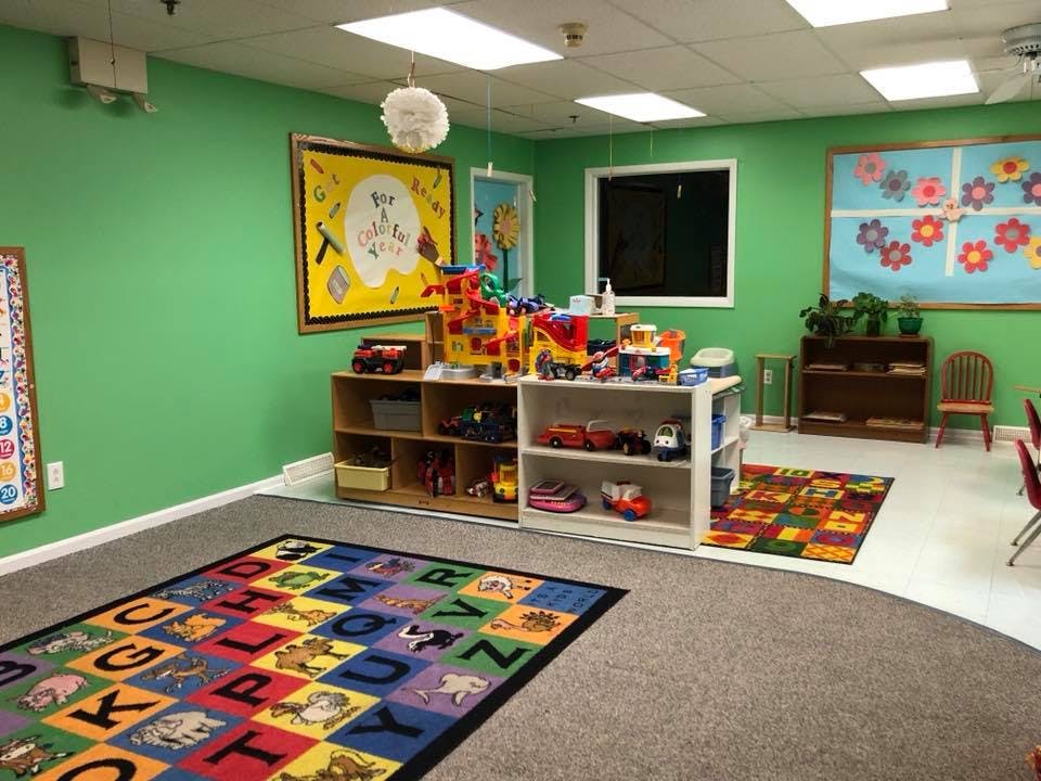 A classroom with green walls, an alphabet rug, and shelves of toys