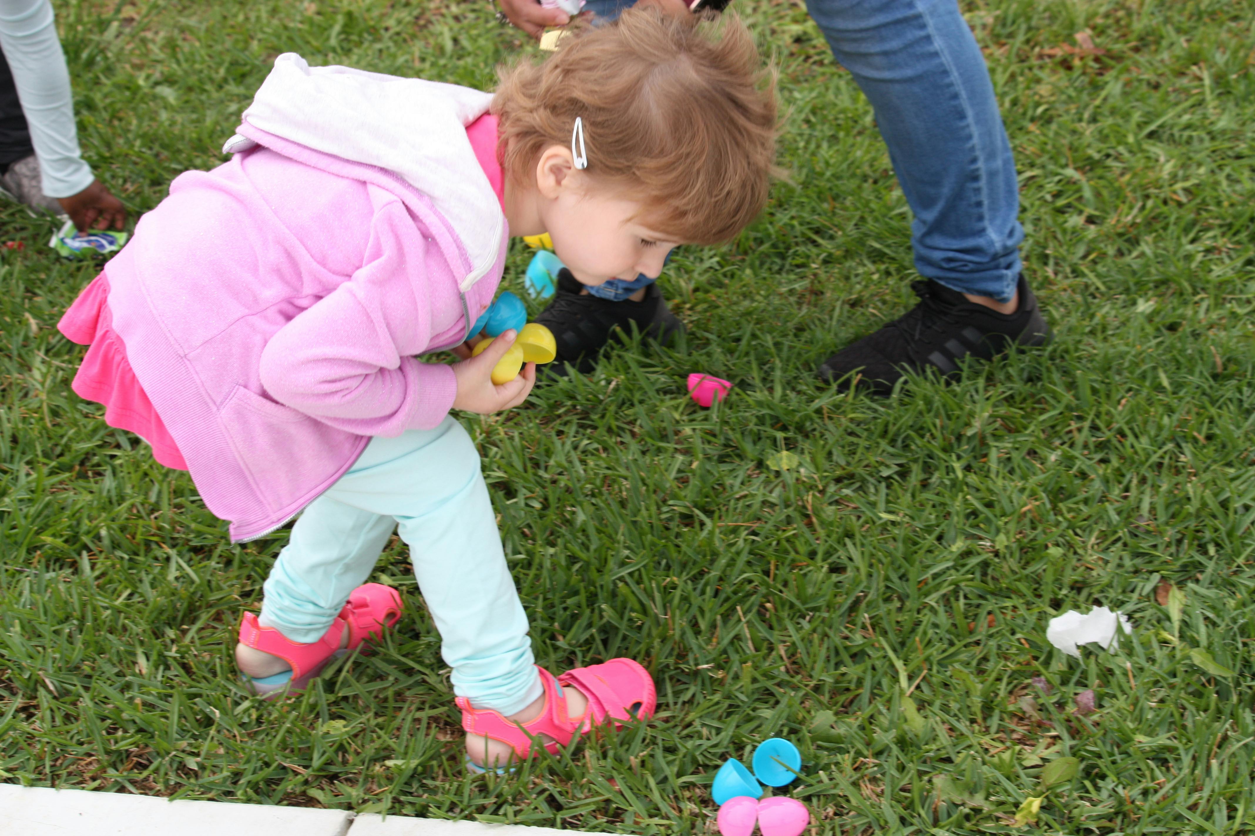 Child picking up plastic eggs on grass during an Easter egg hunt