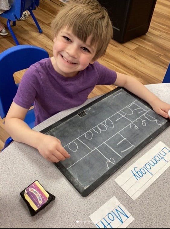 Child at a desk with a small chalkboard and papers