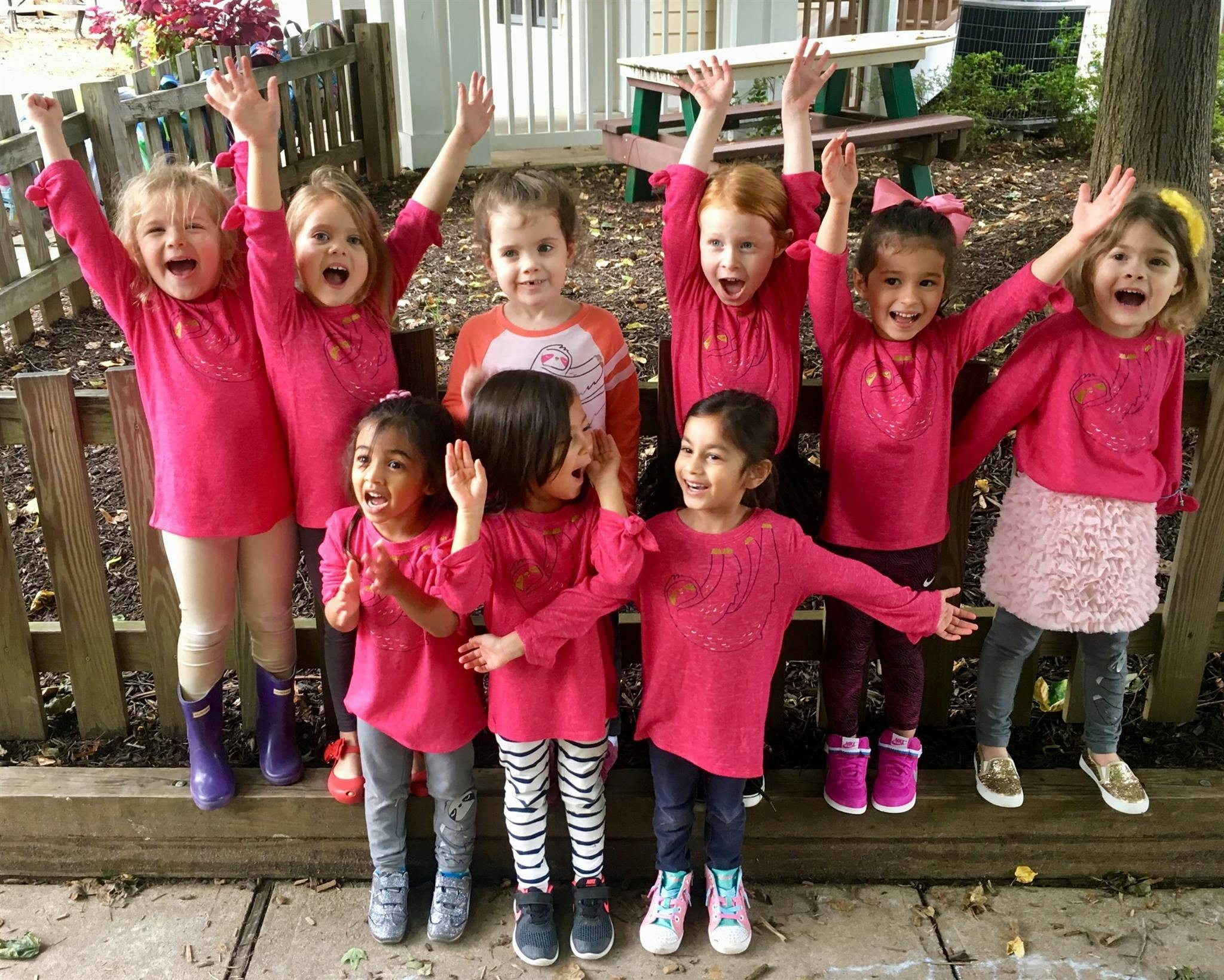 Group of children in pink shirts with arms raised