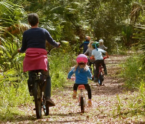 People and children riding bicycles on a dirt path through dense foliage