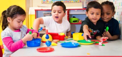 Four children playing with colorful toy dishes at a table