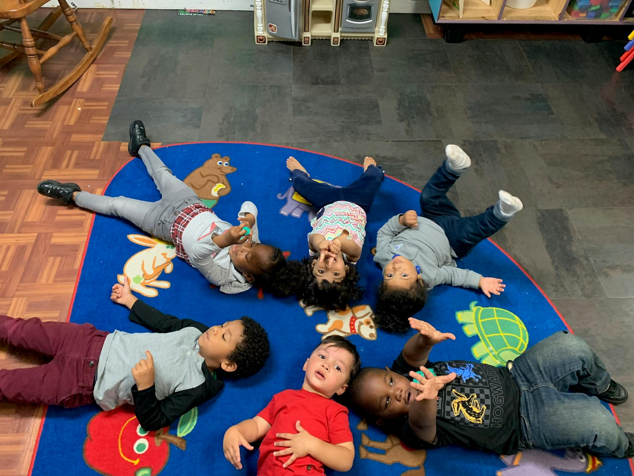 Several children lying on their backs on a blue rug