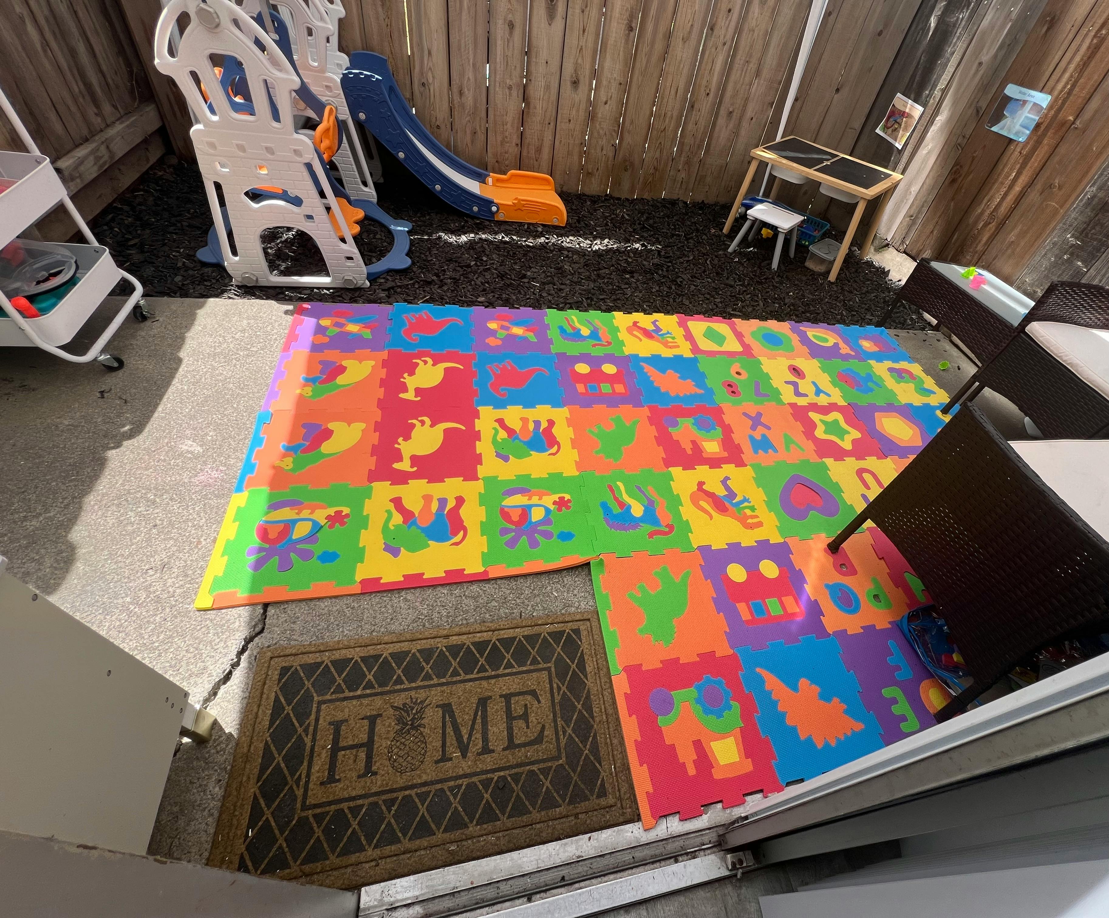 Colorful foam play mat on a patio with a slide and small table