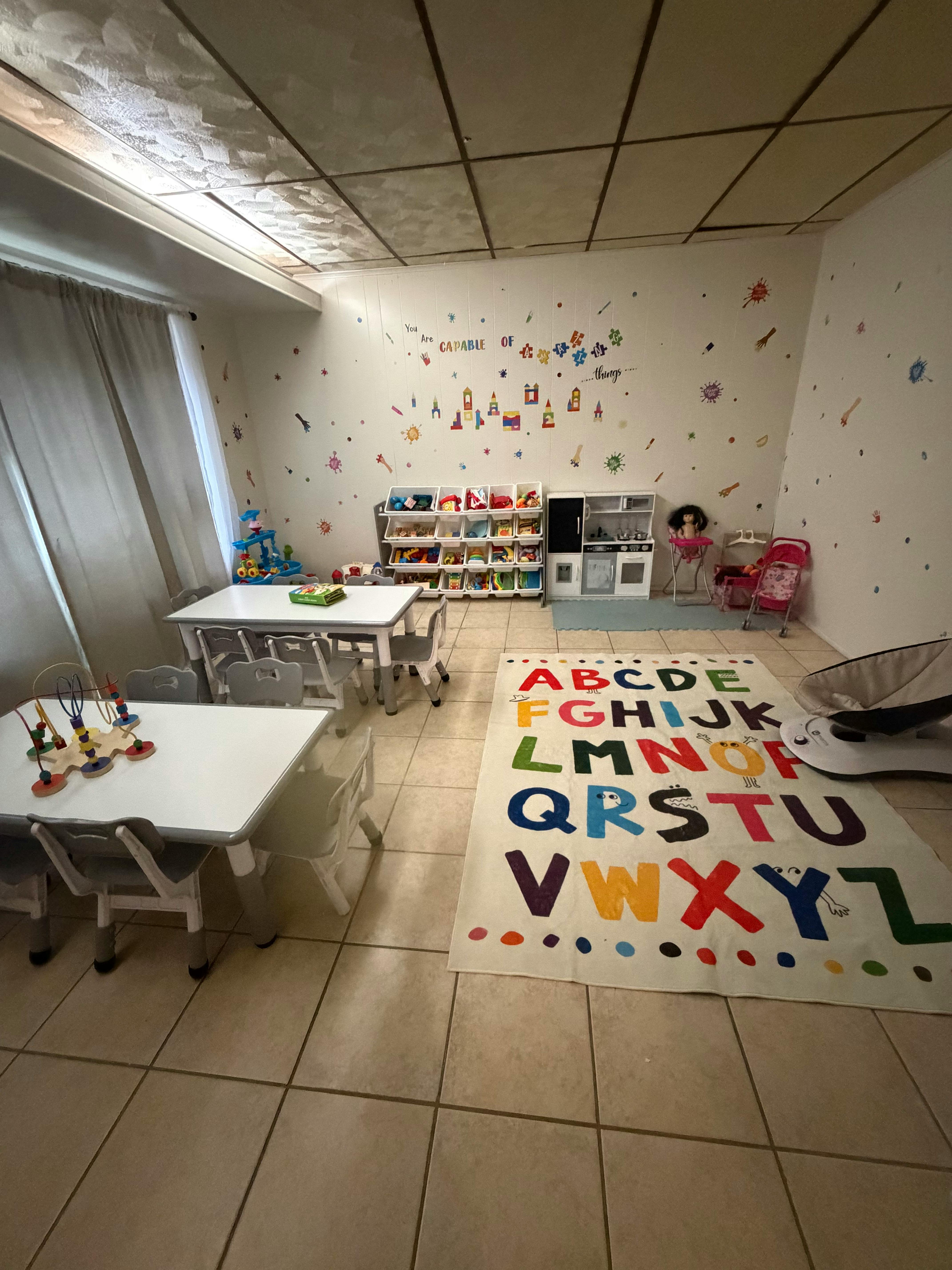 A classroom with small tables and chairs, an alphabet rug, and toys