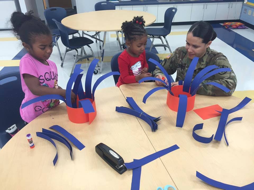 Two children and a person in camouflage making crafts at a table