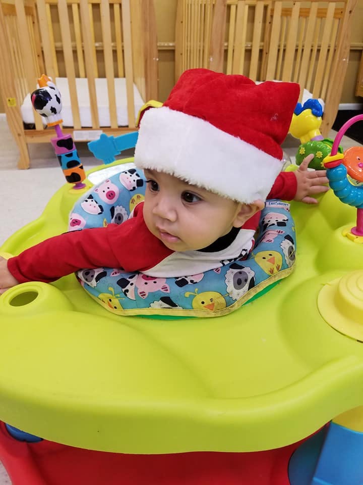 Child in a Santa hat sitting in a baby activity center