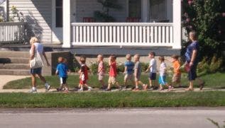 Two adults walking with a line of children on a sidewalk