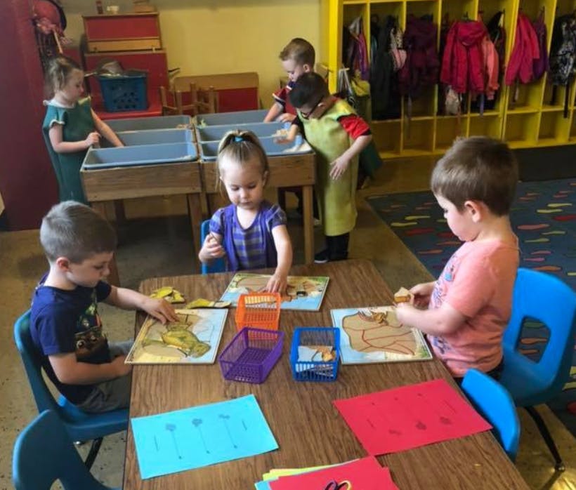 Children playing with puzzles and toys at tables in a classroom