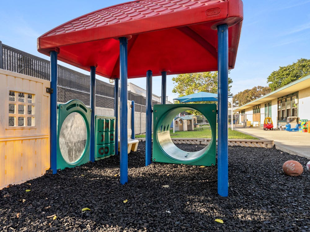 Plastic playground structure with red roof, green tunnel, and mirror wall