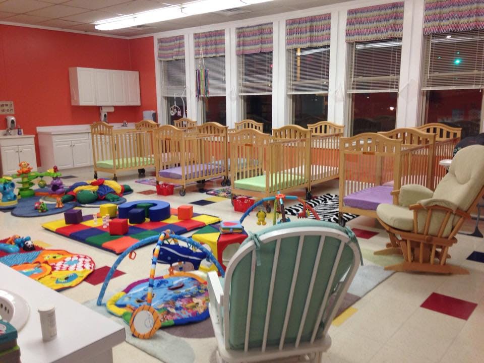 Nursery room with multiple cribs, play mats, and a rocking chair