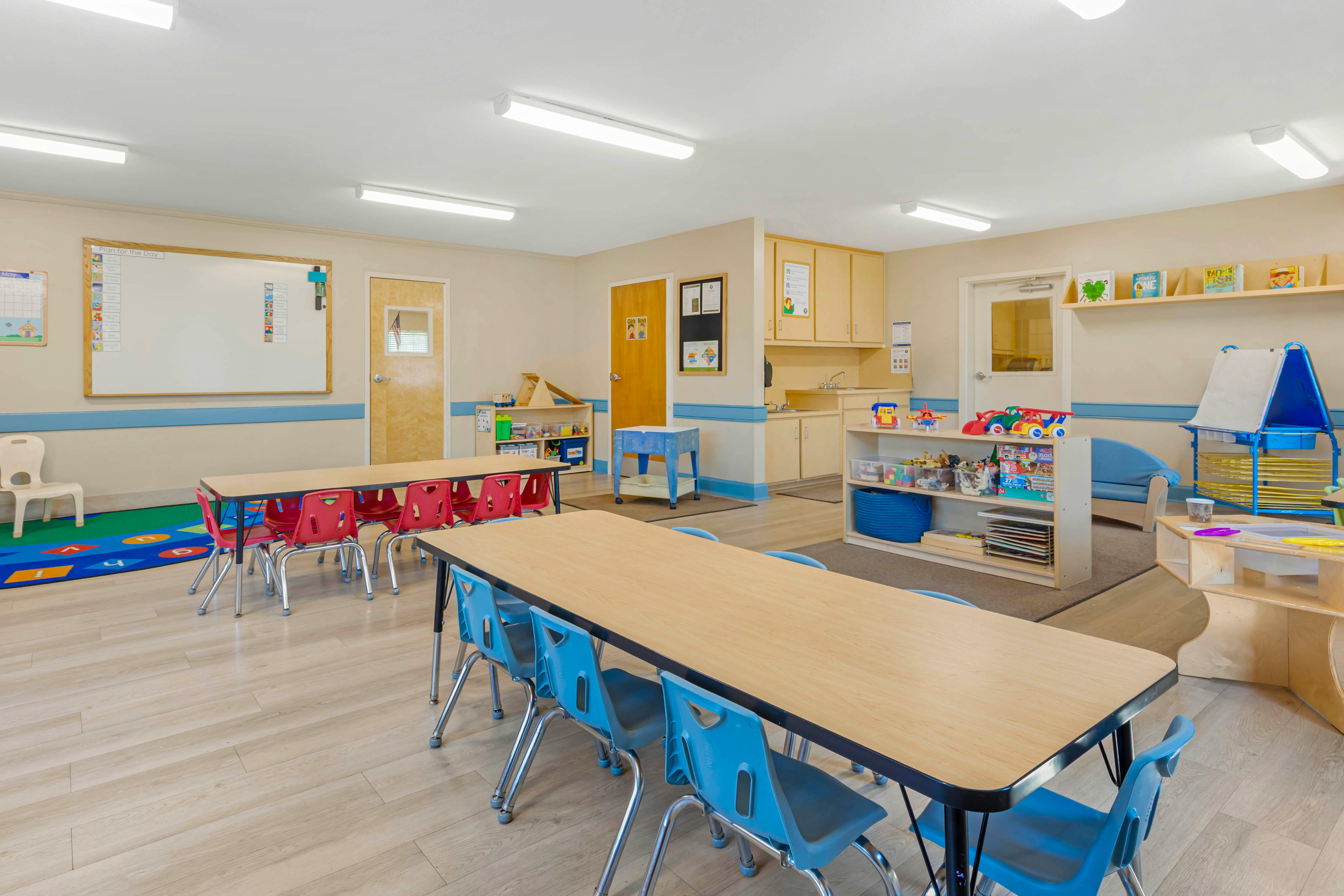 An empty children's classroom with several tables and chairs, toys, and whiteboards