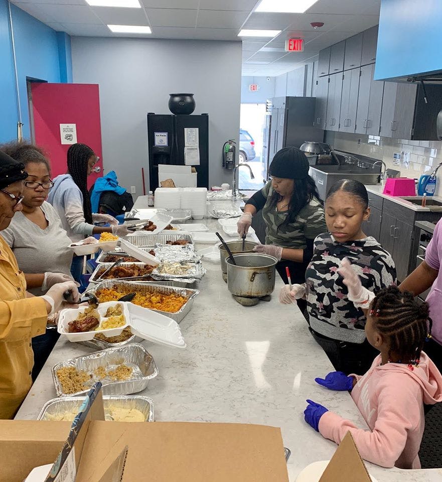 People serving food into containers in a kitchen
