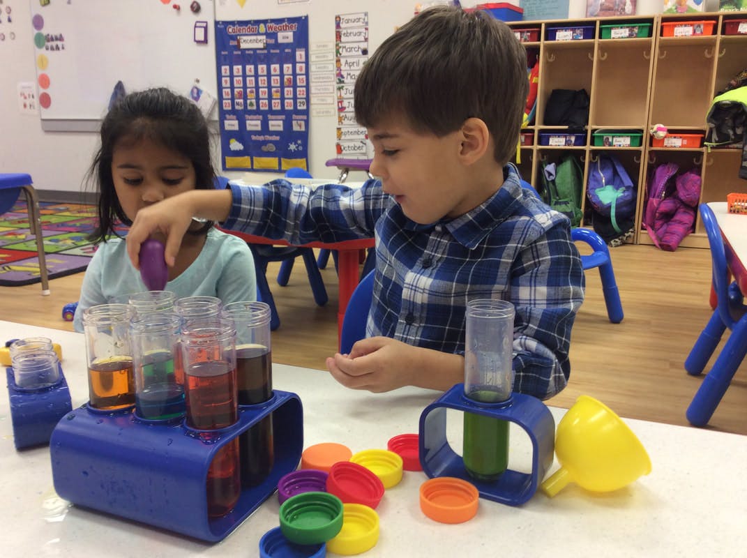 Two children playing with colorful liquids in a classroom