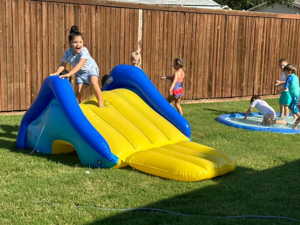 Child standing on an inflatable slide in a yard with other children