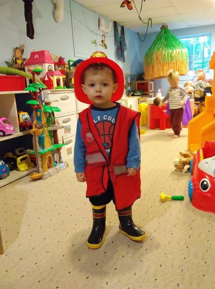 Child in a red vest and hat standing in a room with toys