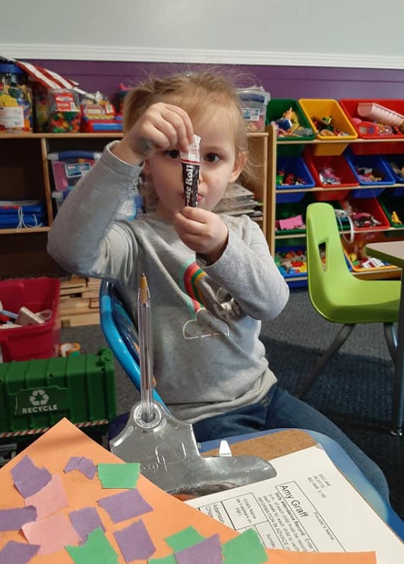 Child holding up a glue stick in a classroom