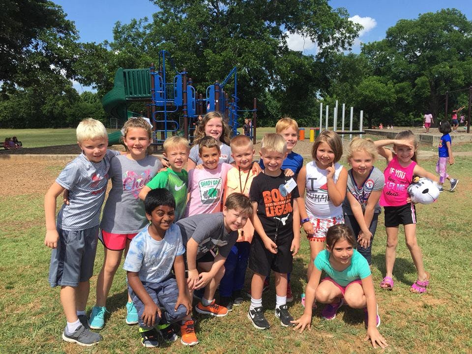 Group of children posing on a grassy field with a playground in the background