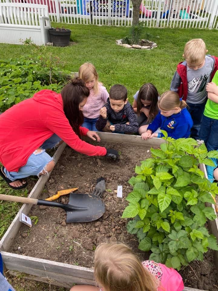 Person and children planting in a garden bed