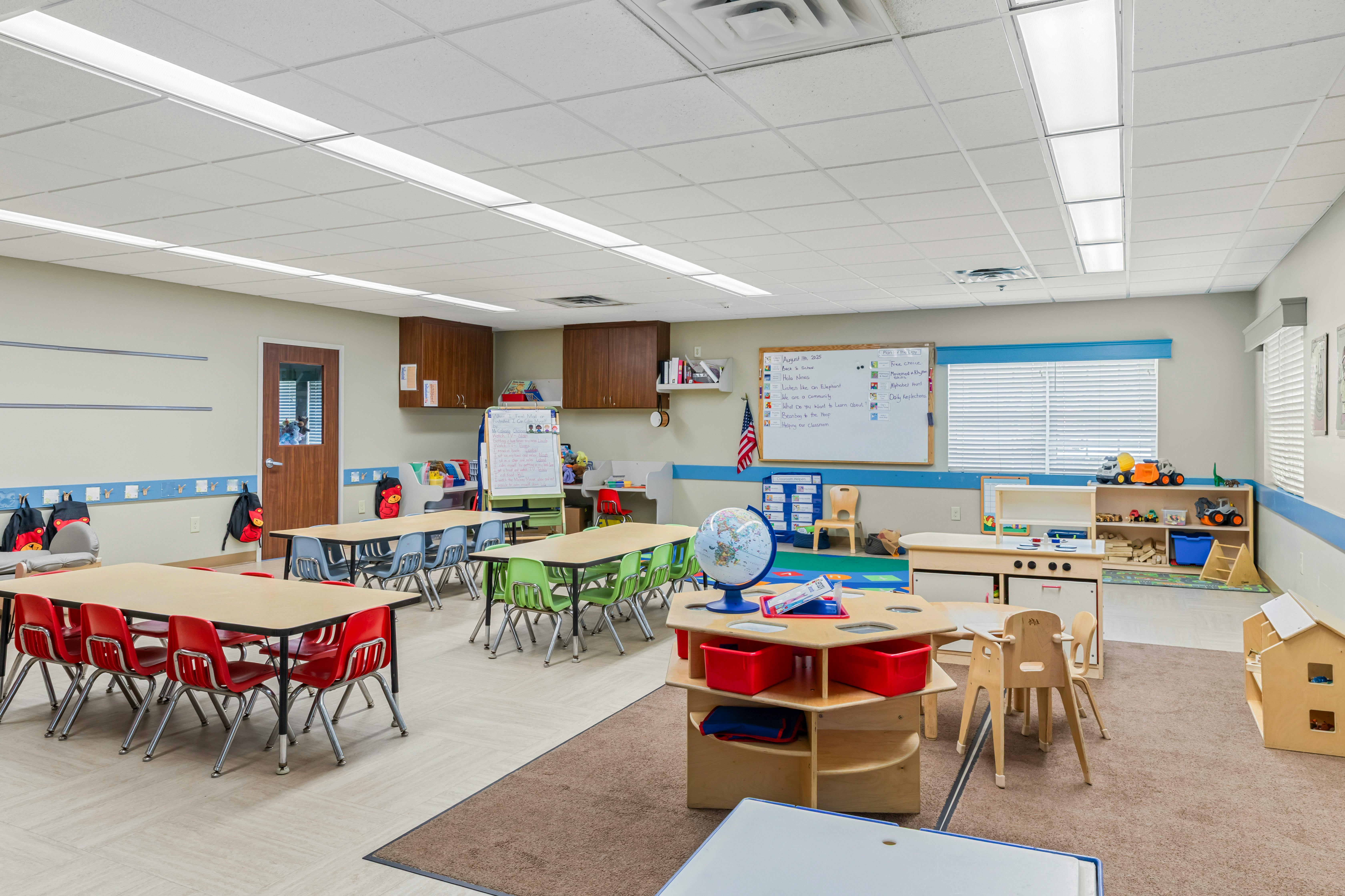 An empty classroom with small tables and chairs, and a whiteboard with activities