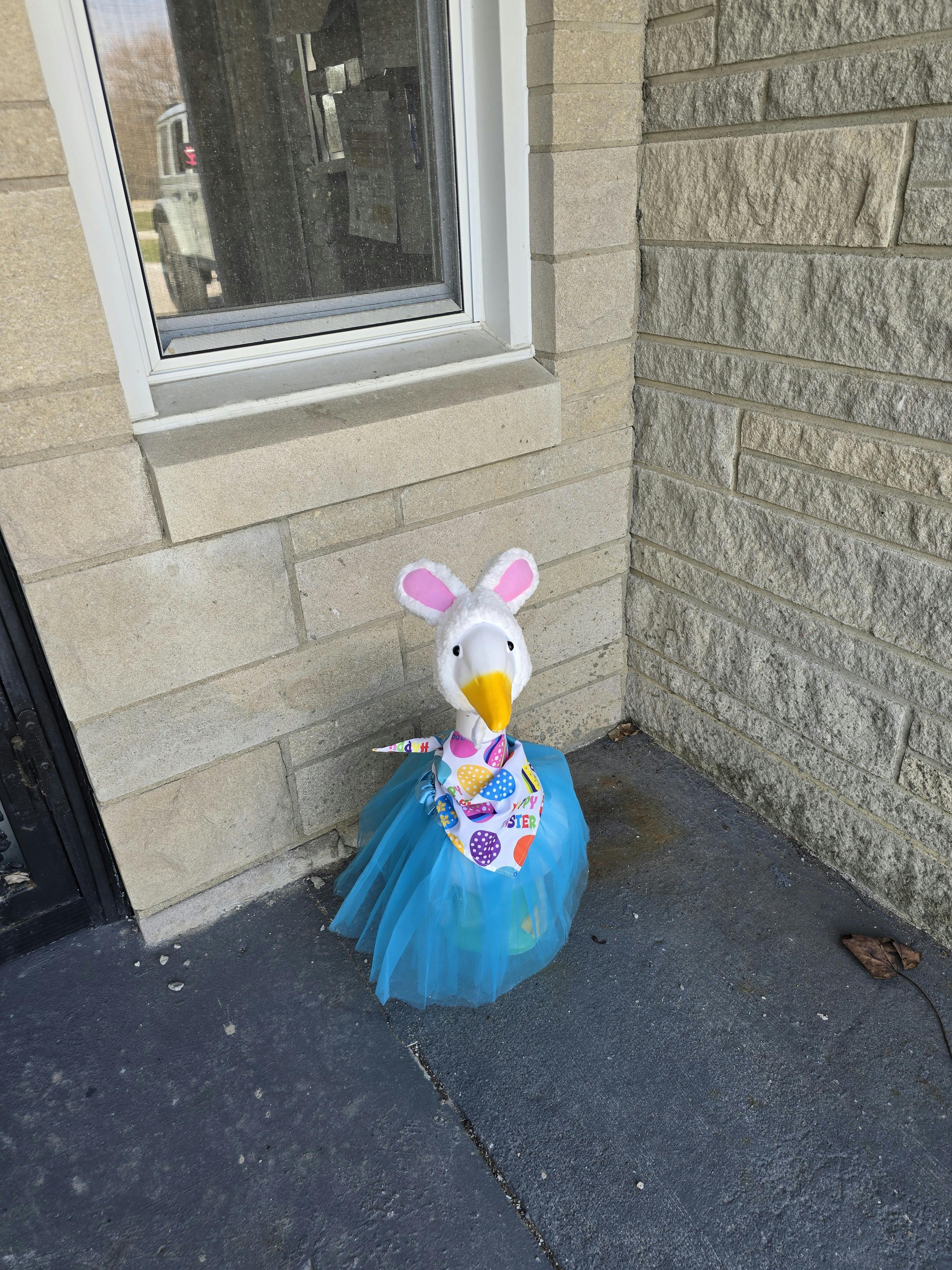 Decorative goose statue wearing bunny ears, a blue tutu, and an Easter bandana