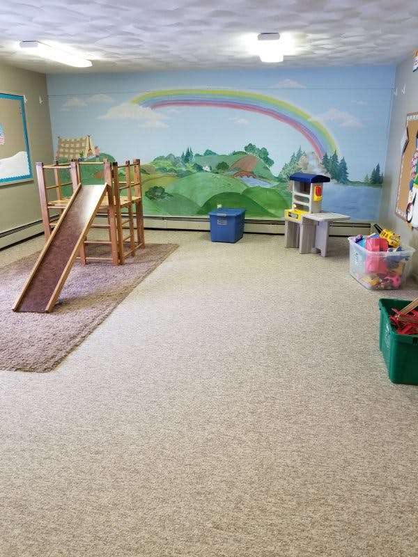 Indoor play area with a wooden slide and a rainbow mural on the wall
