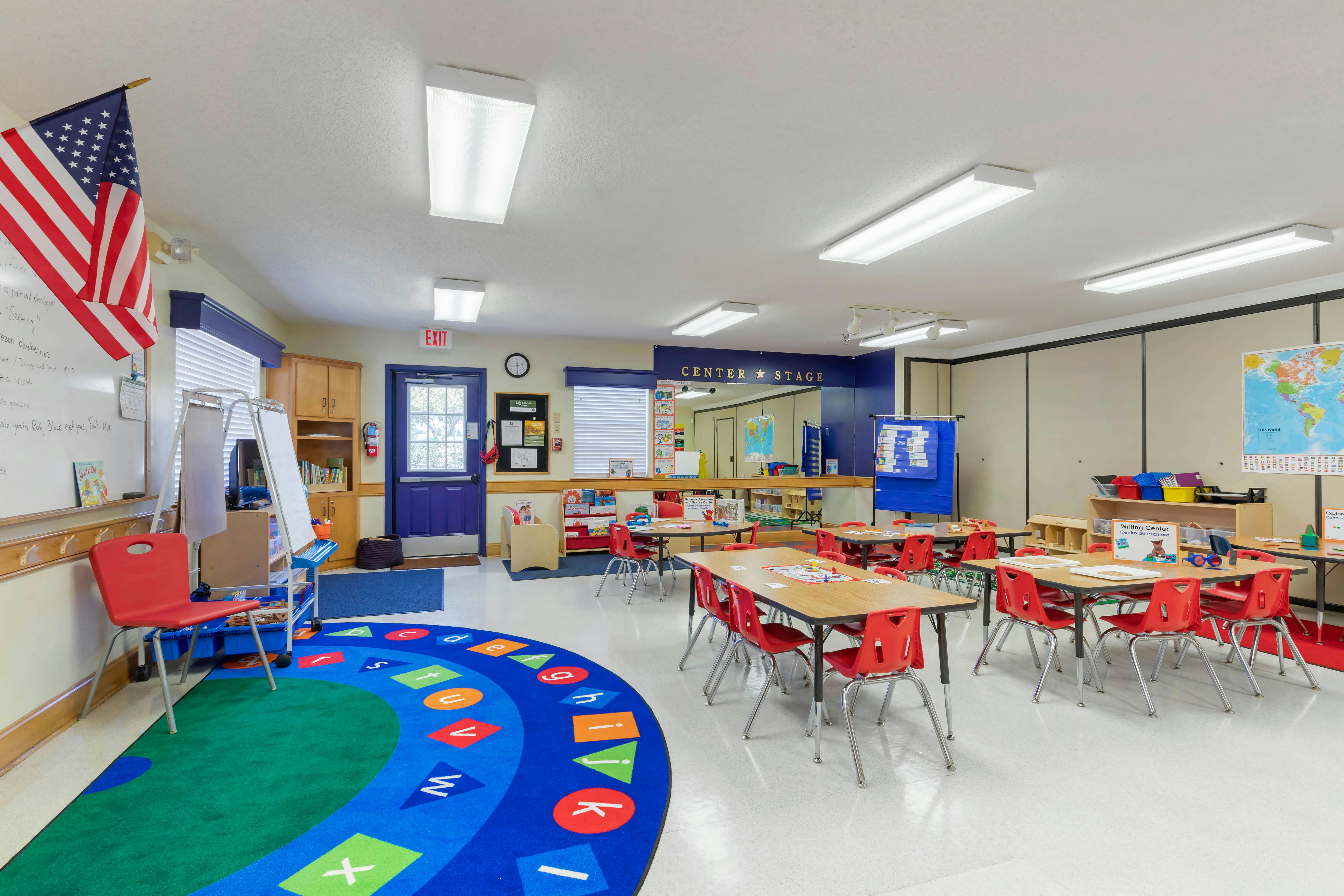 Classroom with tables, red chairs, an alphabet rug, and teaching aids