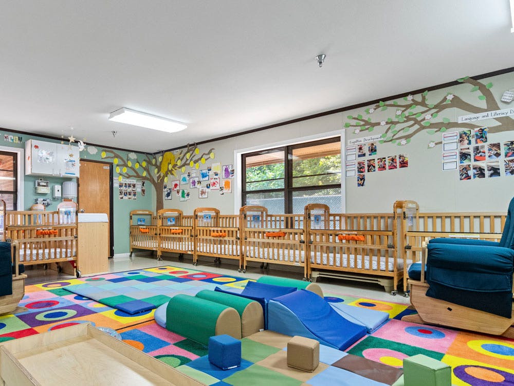 A colorful play area with cribs and soft play equipment in a daycare classroom