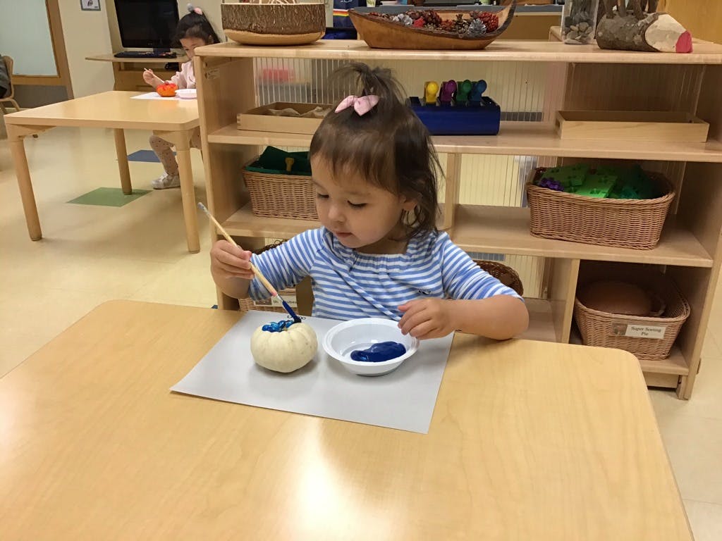 Child painting a small white object blue at a table