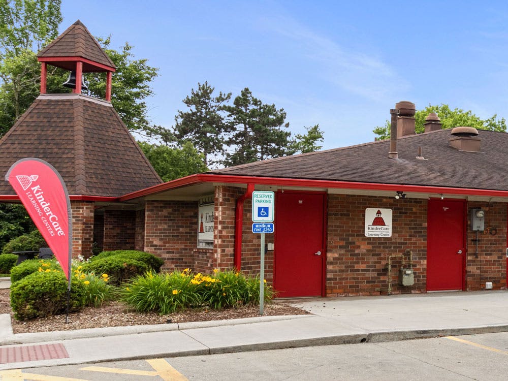 Brick building with red trim and doors, bell tower, and a KinderCare flag